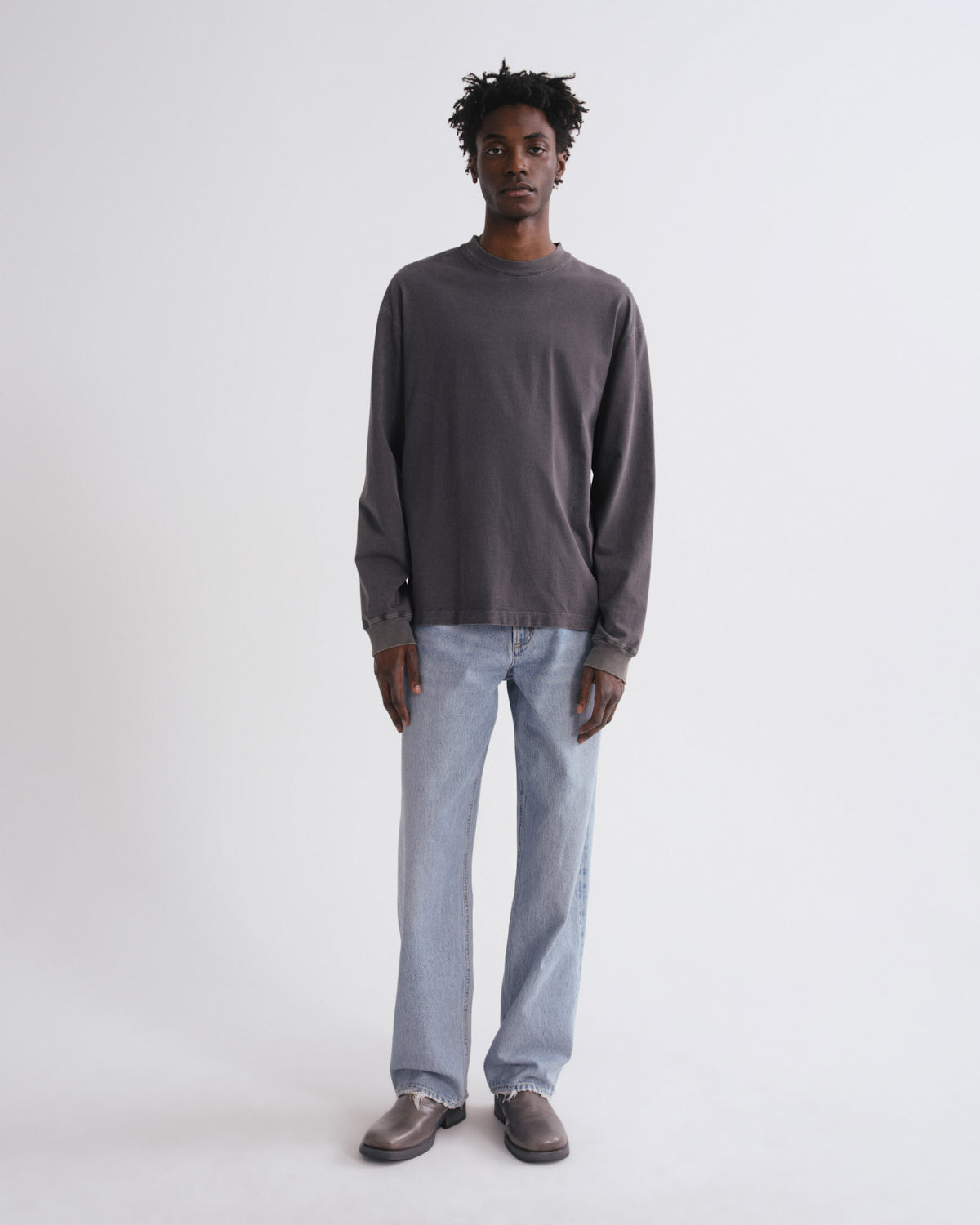 Man wearing a dark gray long-sleeve shirt and light blue jeans on a white background