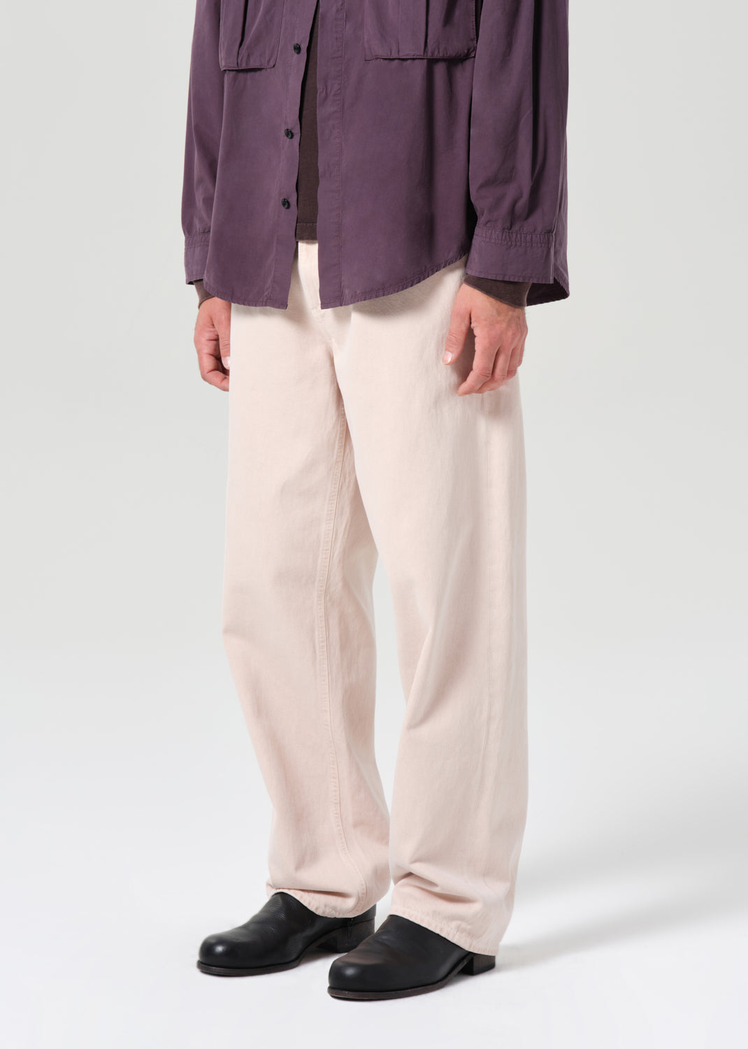 Person wearing a purple jacket, beige pants, and black shoes on a white background