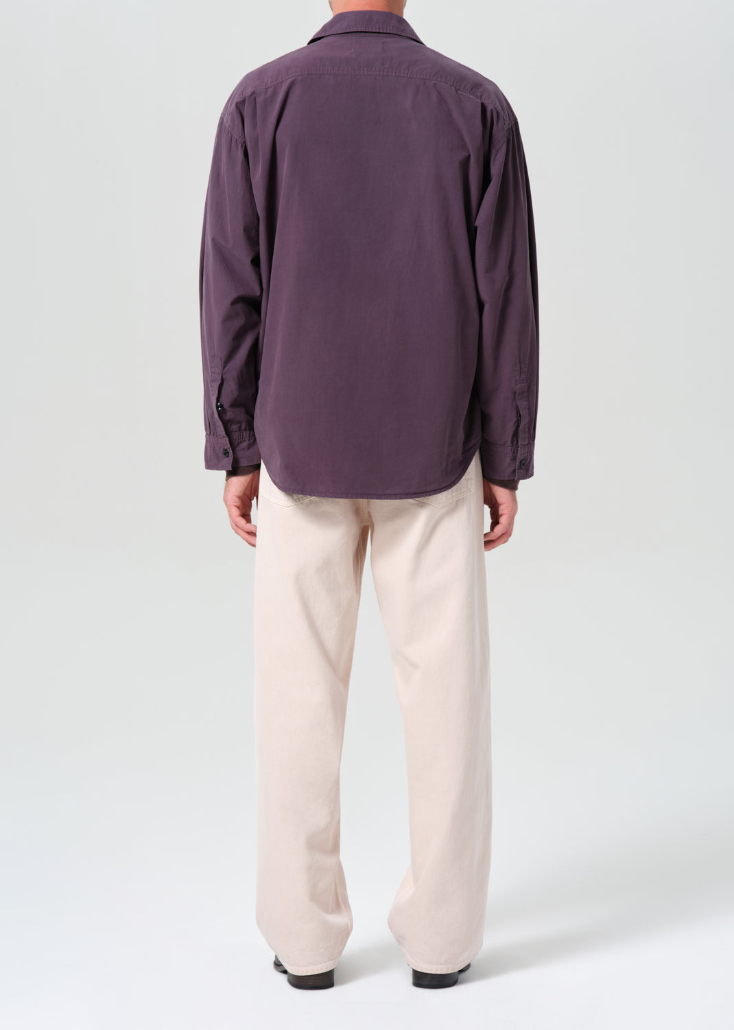 Person wearing a purple shirt and beige pants on a white background