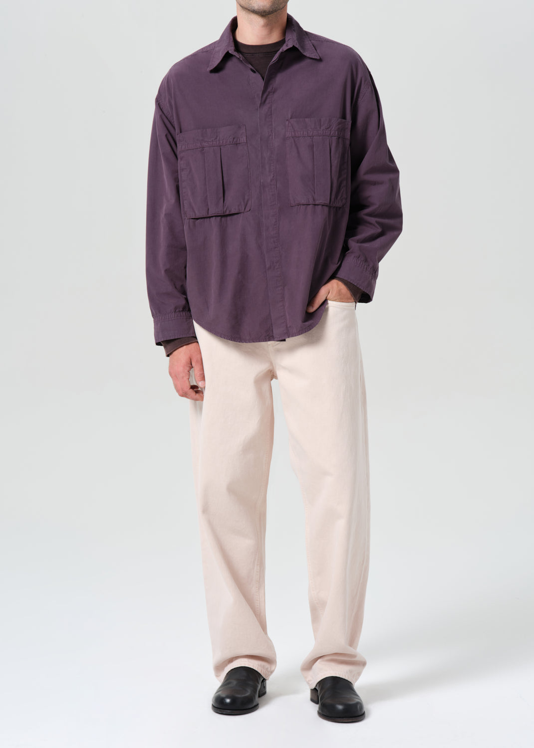Person wearing a purple shirt and beige pants on a white background