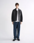Person wearing a black leather jacket with blue jeans and black shoes on a grey background