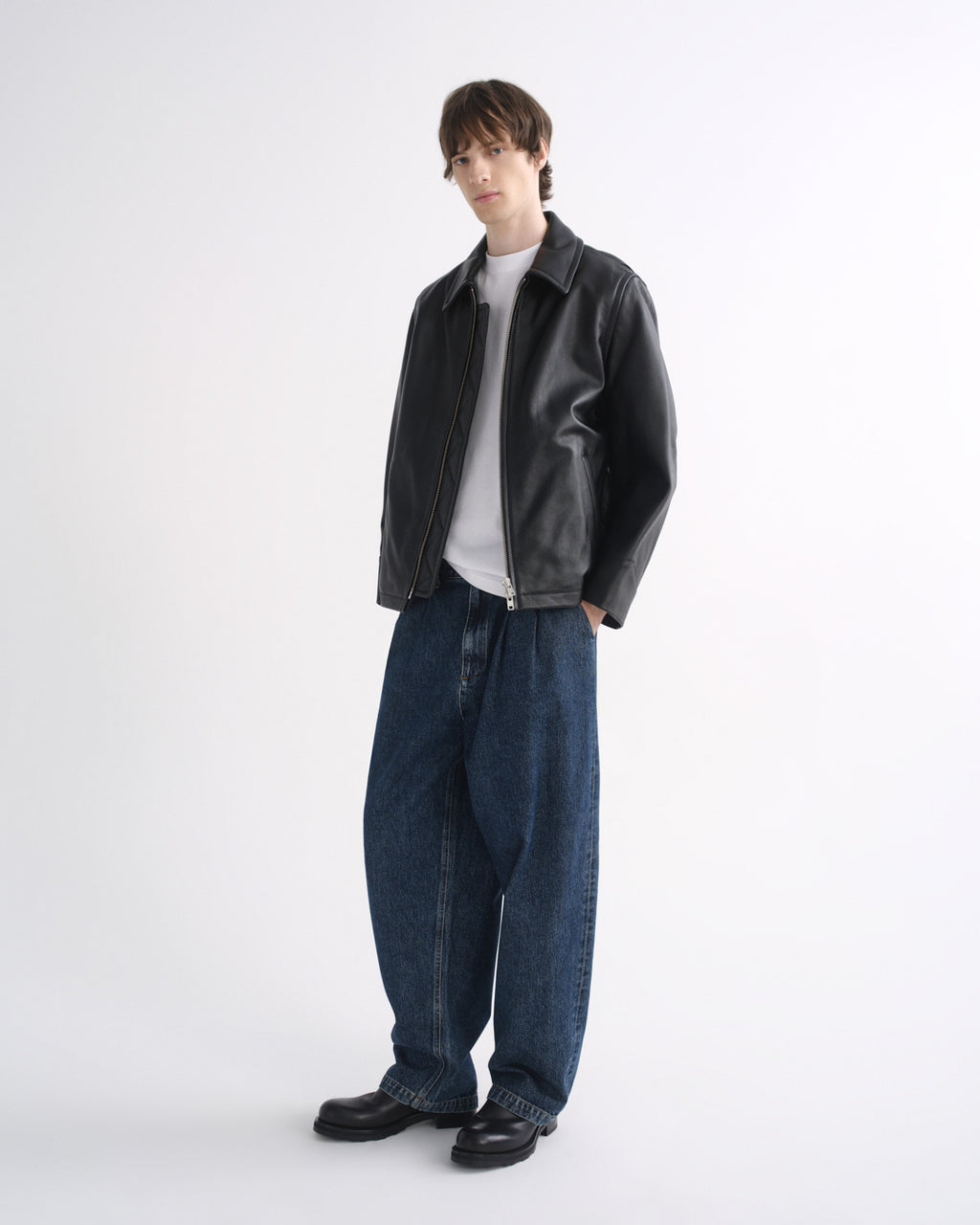 Person wearing a black leather jacket with blue jeans and black shoes on a grey background