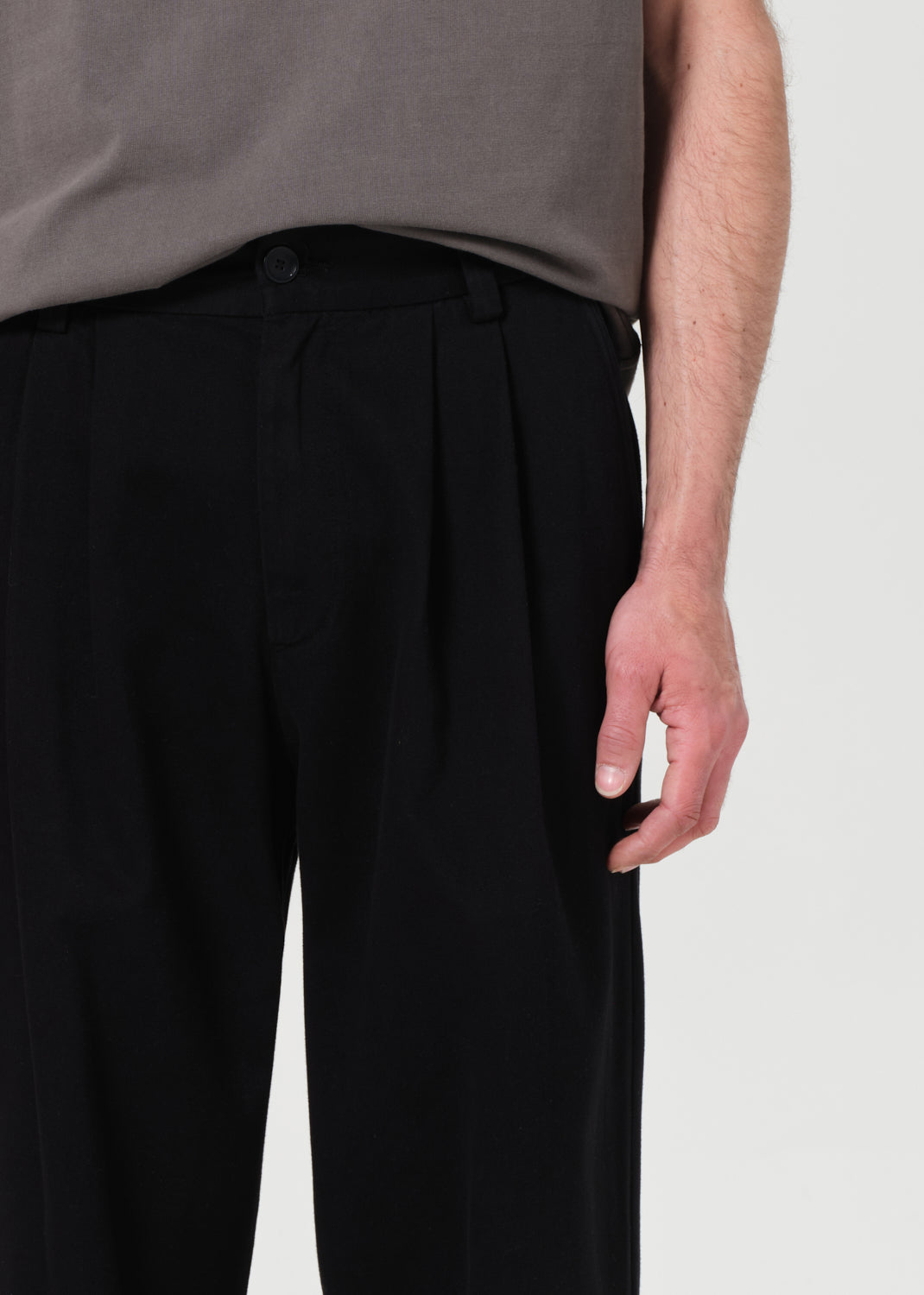 Person wearing black pleated pants with a plain background