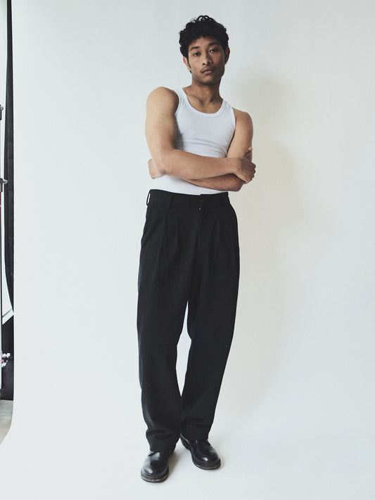 Man wearing a white tank top and black pants standing against a white background