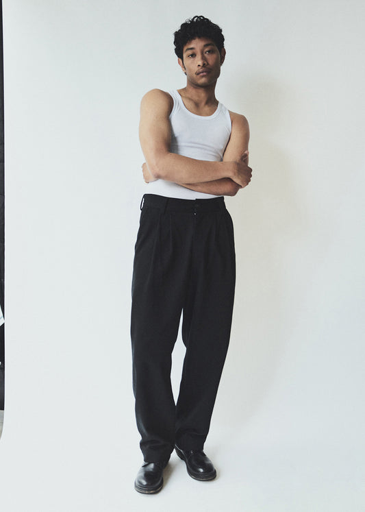 Man wearing a white tank top and black pants standing against a plain background