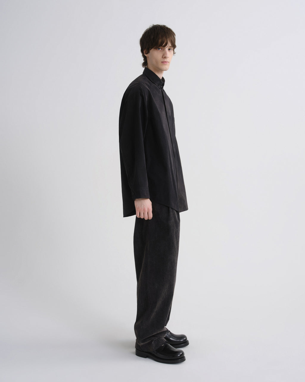 Person wearing a black suit standing against a white background