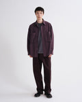 Person wearing a dark purple shirt and pants on a grey background