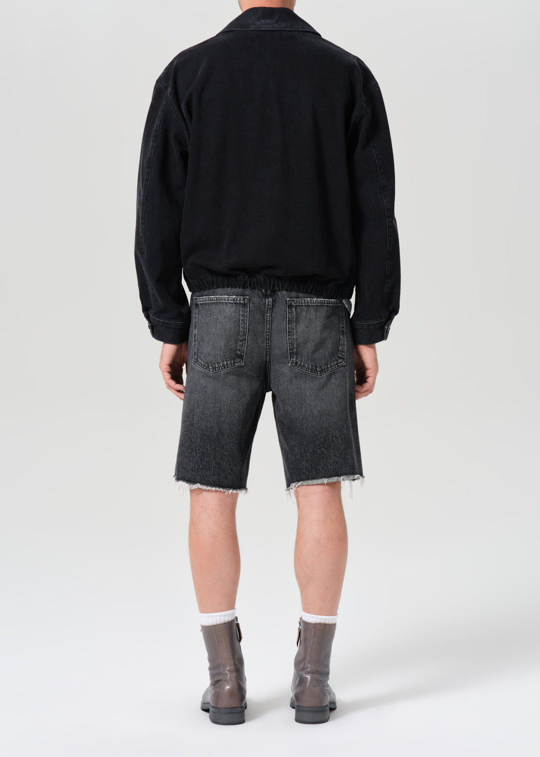 Person wearing a black jacket and gray shorts on a white background