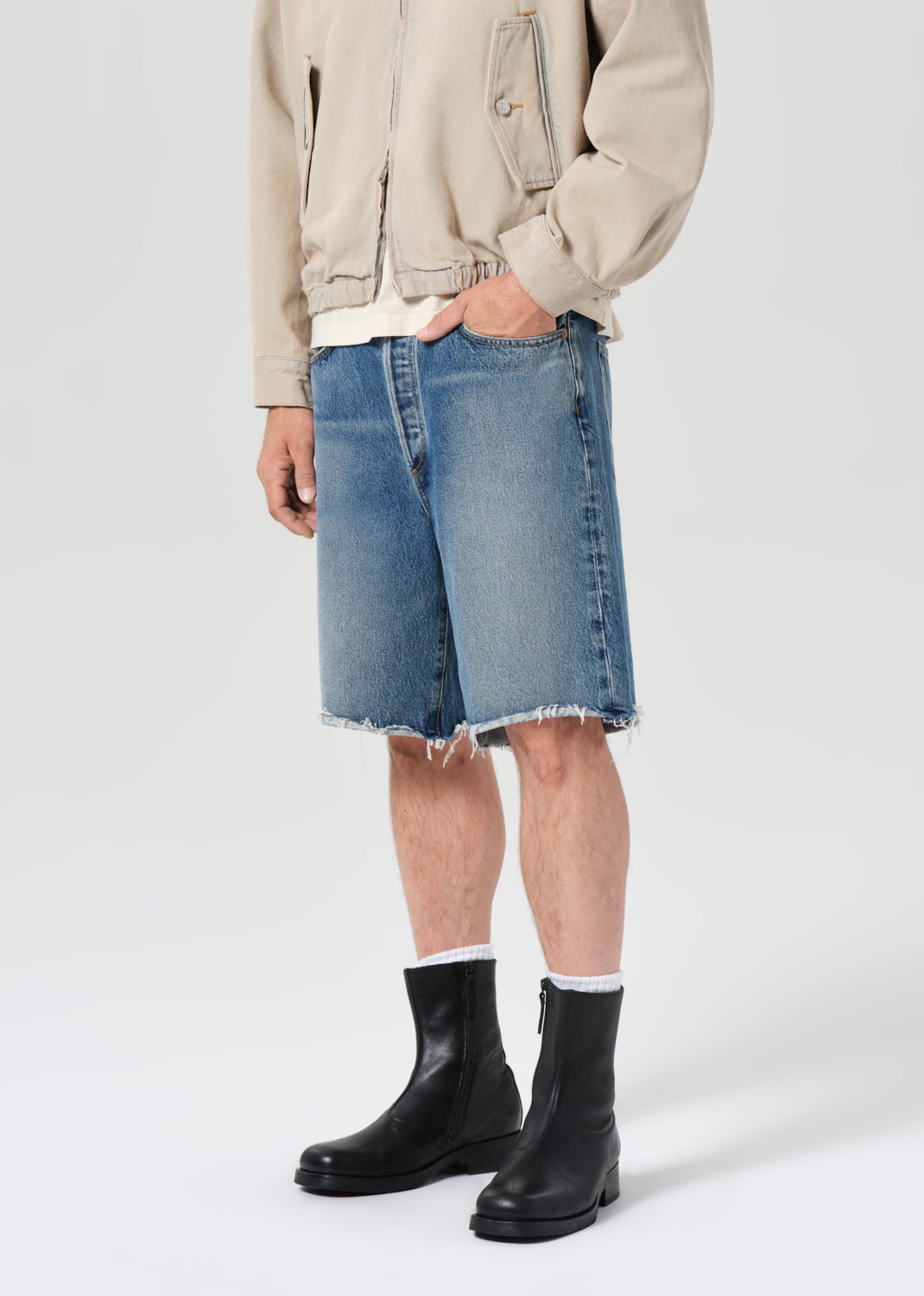 Person wearing a beige jacket, blue denim skirt, and black boots on a white background