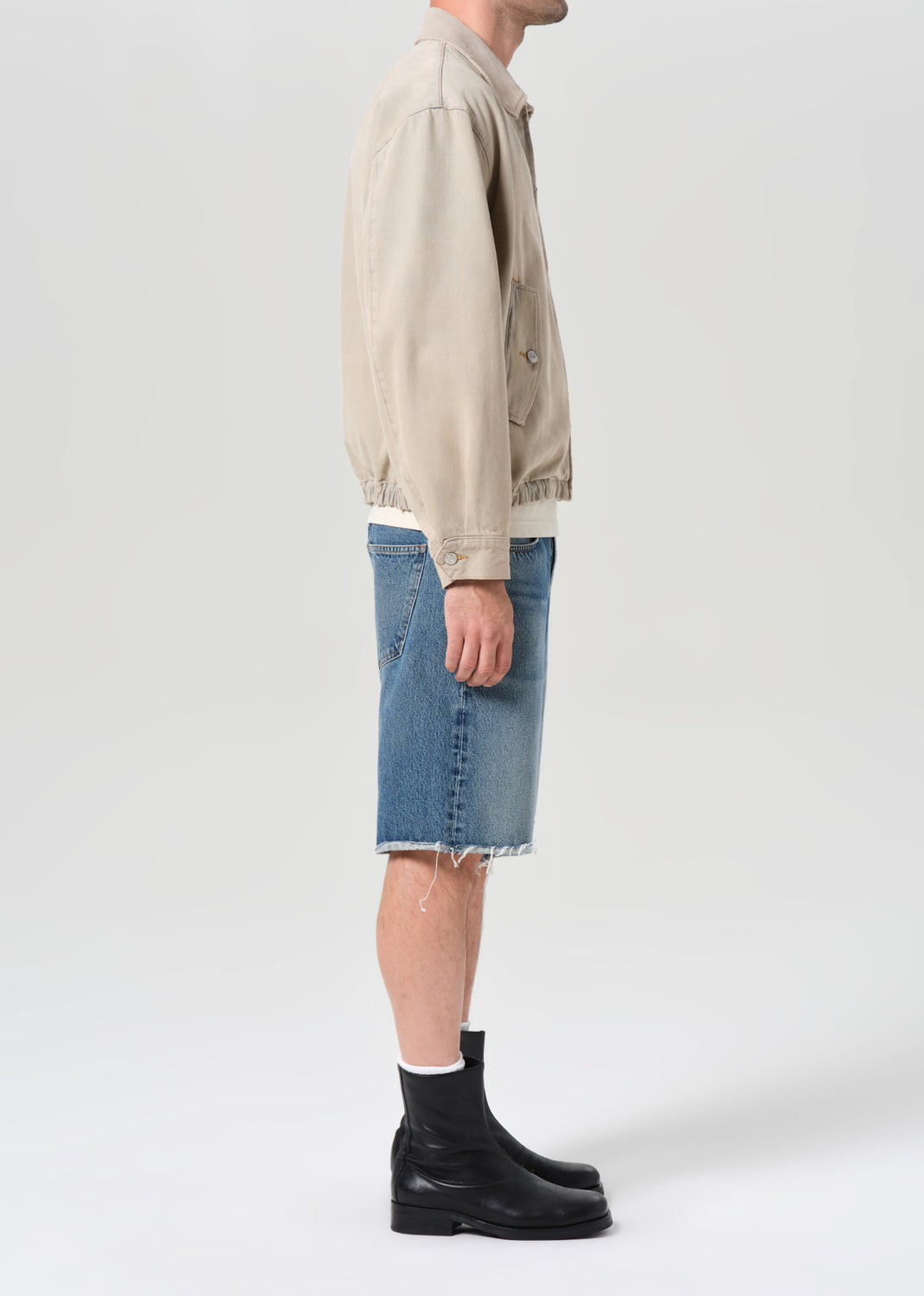 Person wearing a beige jacket, blue jeans, and black shoes on a white background