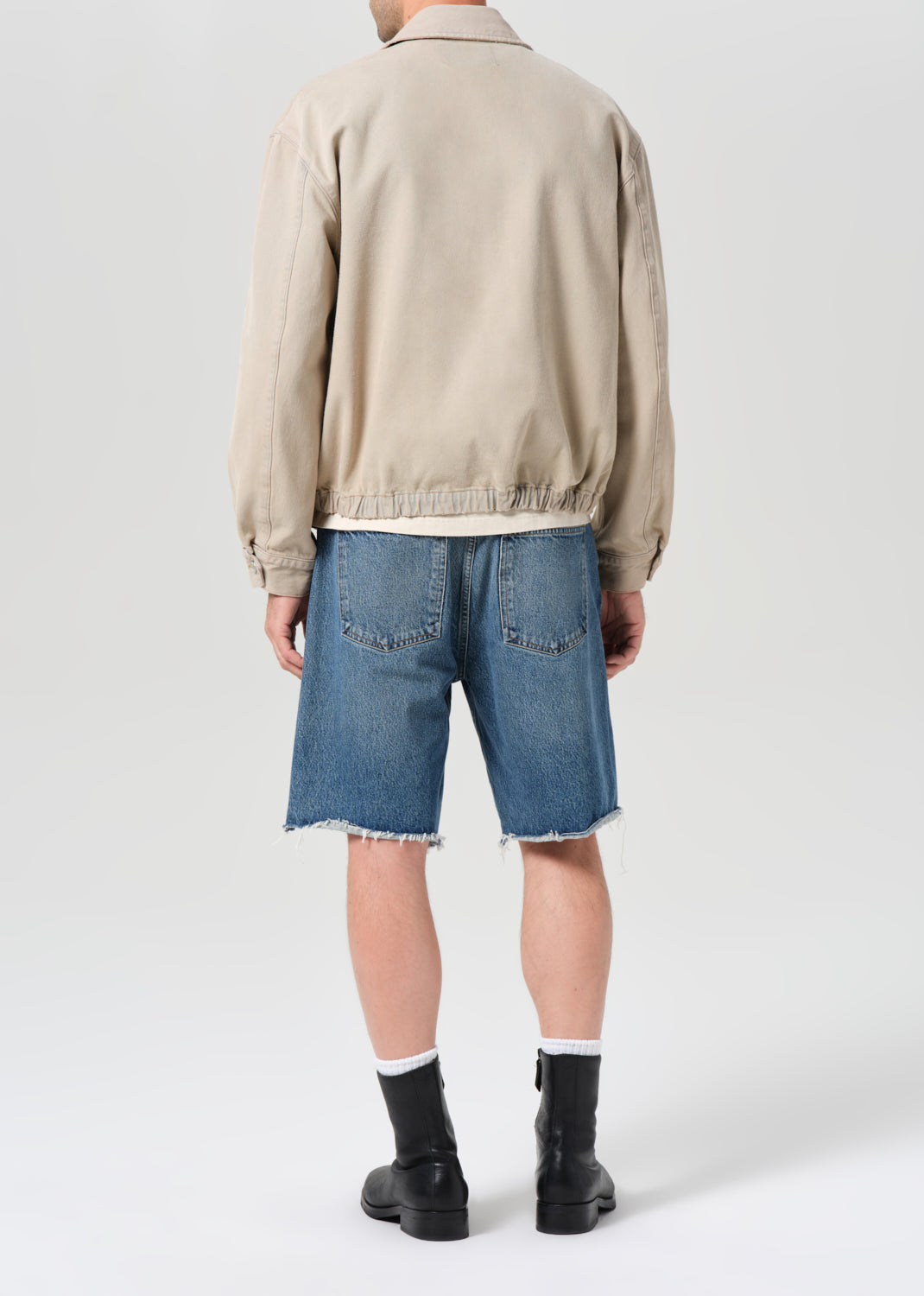 Person wearing a beige jacket and blue denim shorts on a white background