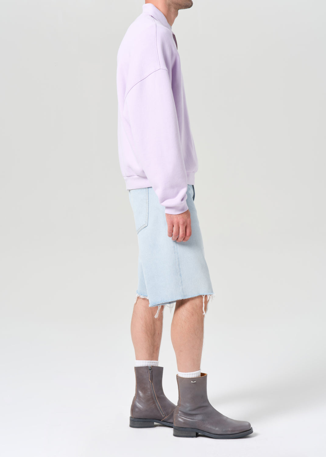 Person wearing a light purple shirt, light blue shorts, and gray rain boots on a white background