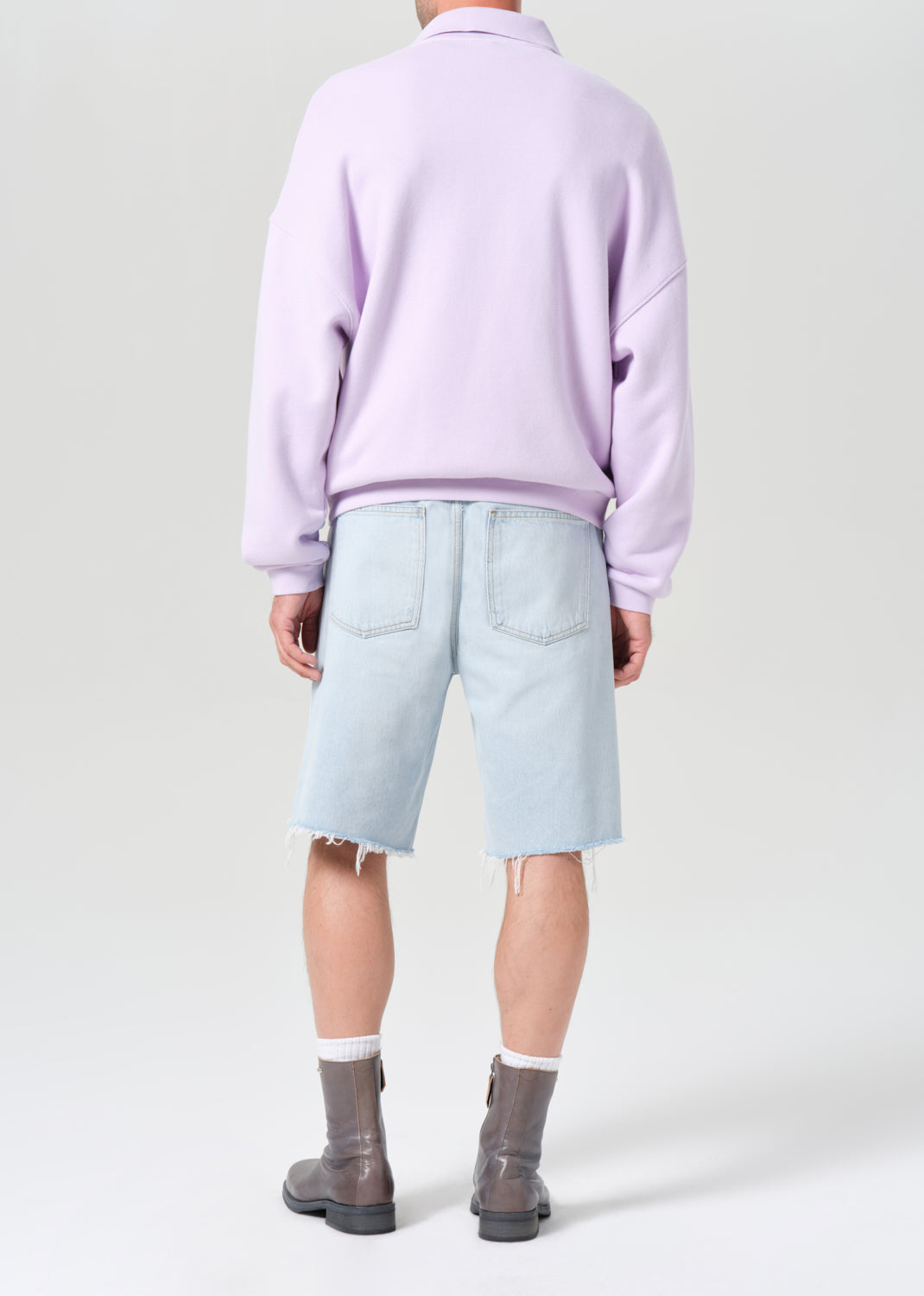 Person wearing a light purple sweater, light blue shorts, and gray boots on a white background