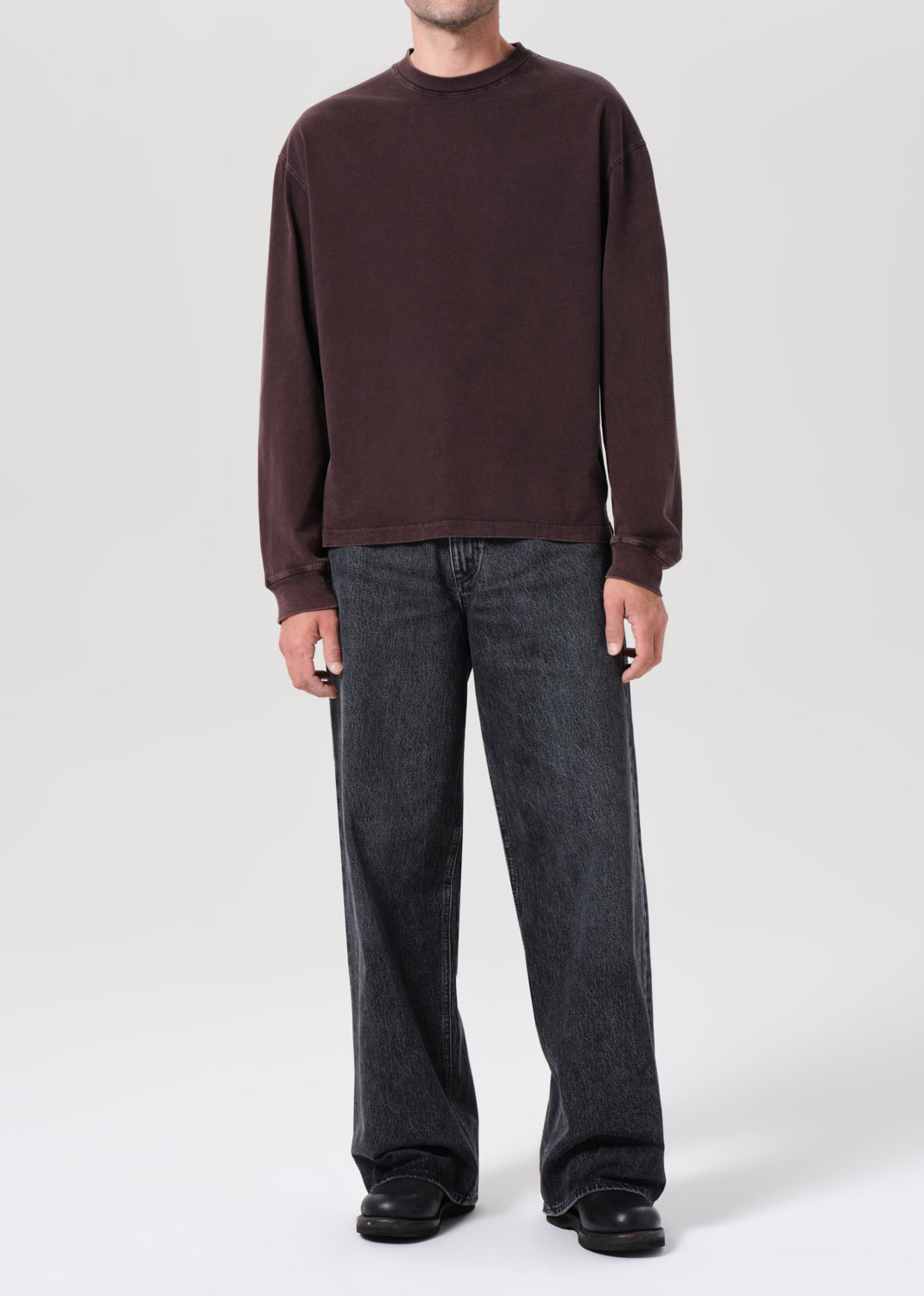 Person wearing a brown long-sleeve shirt and dark jeans on a white background