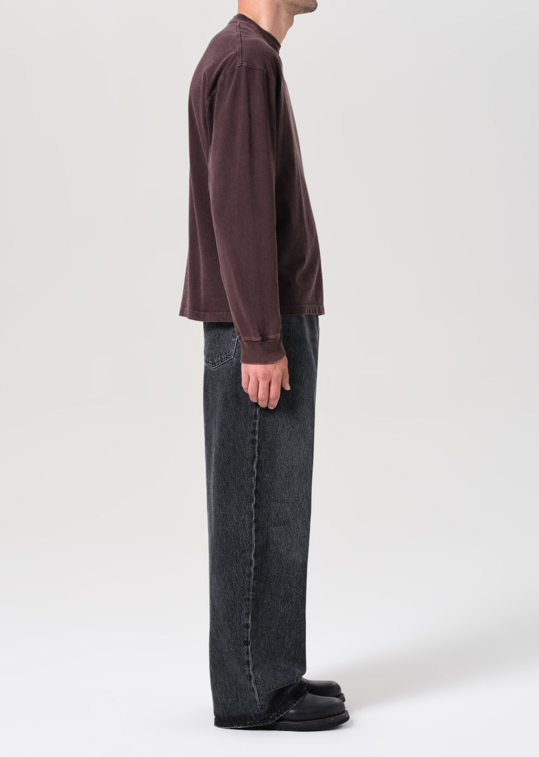 Person wearing a brown long-sleeve shirt and dark jeans on a white background