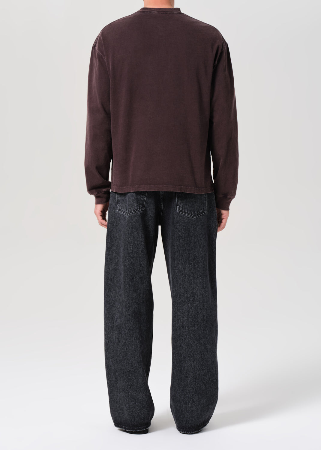 Person wearing a brown long-sleeve shirt and dark jeans on a white background