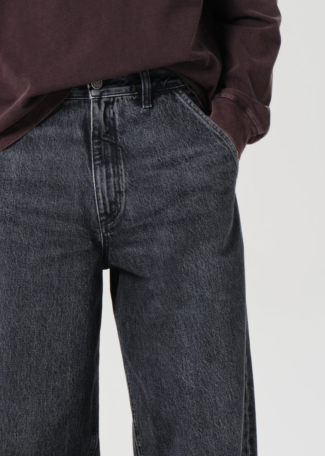 Person wearing dark jeans and a maroon shirt on a light background