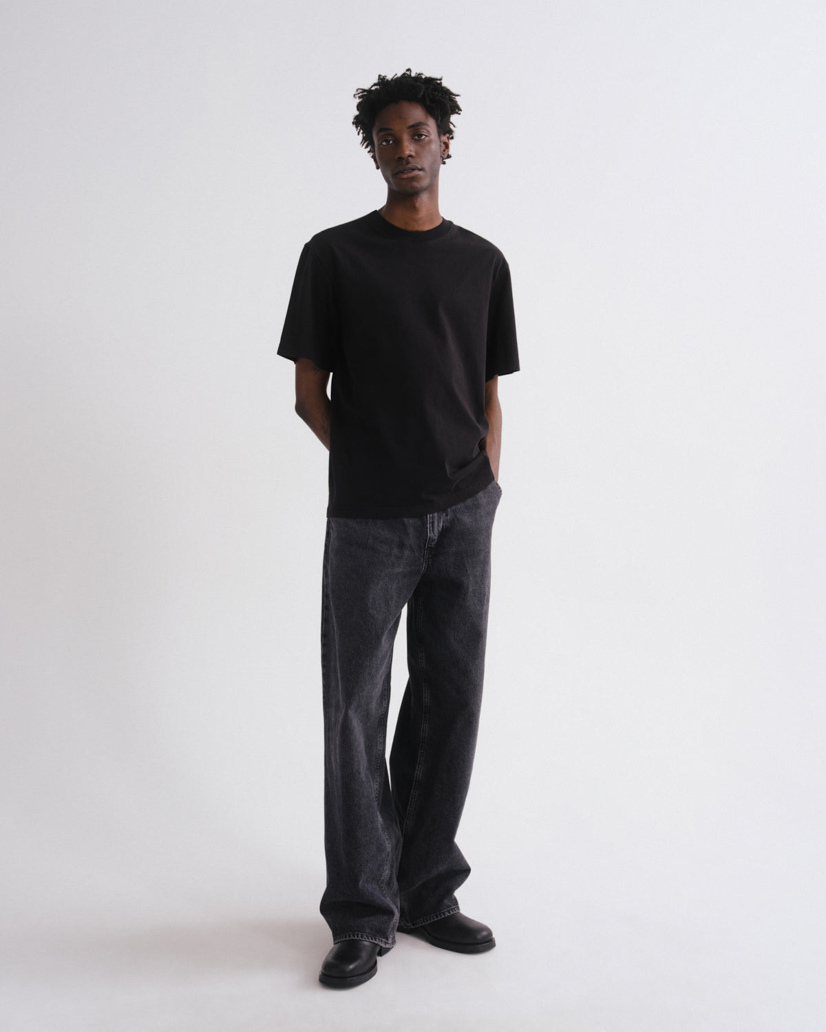 Person wearing a black t-shirt and dark jeans on a white background