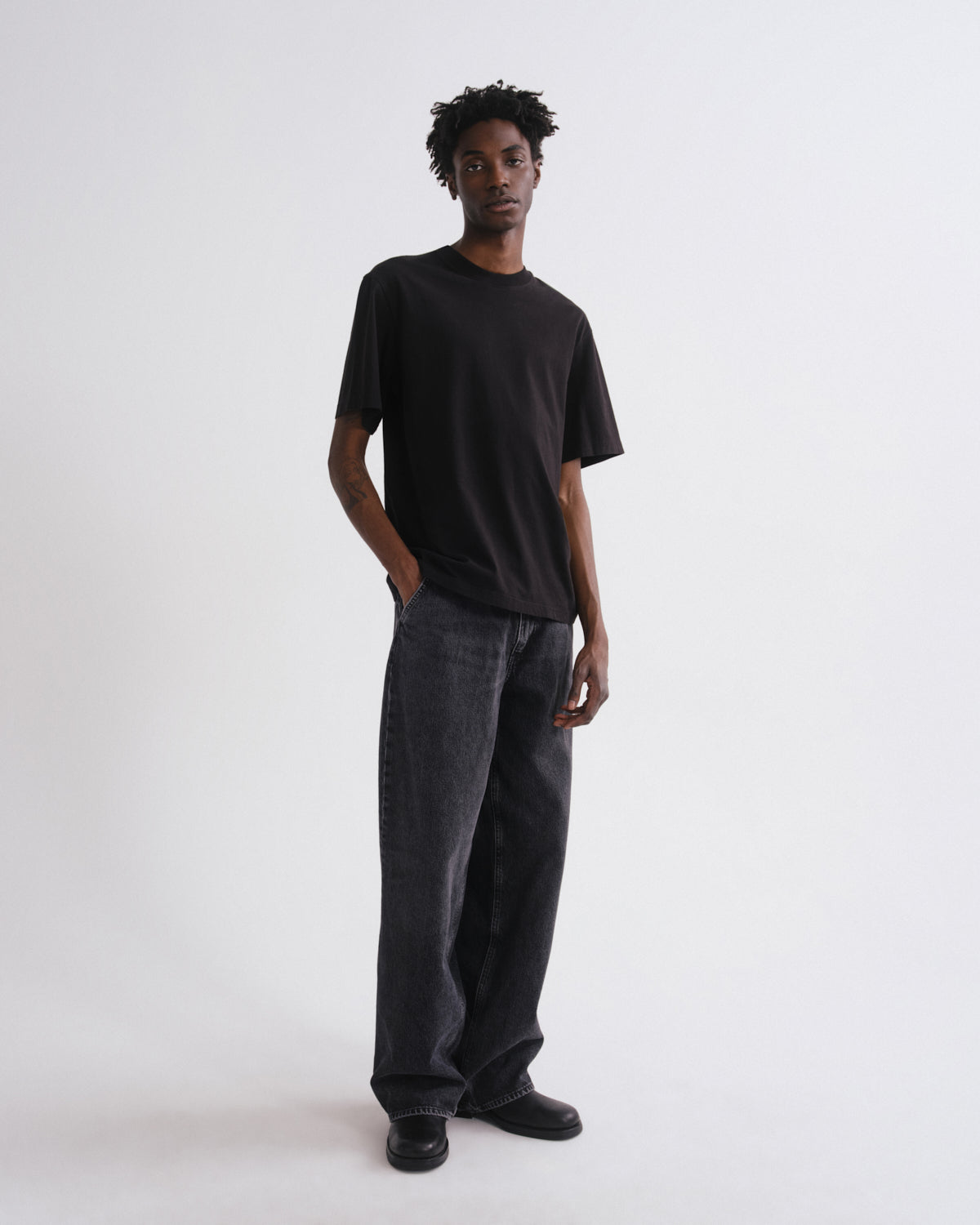 Person wearing a black t-shirt and dark jeans on a white background