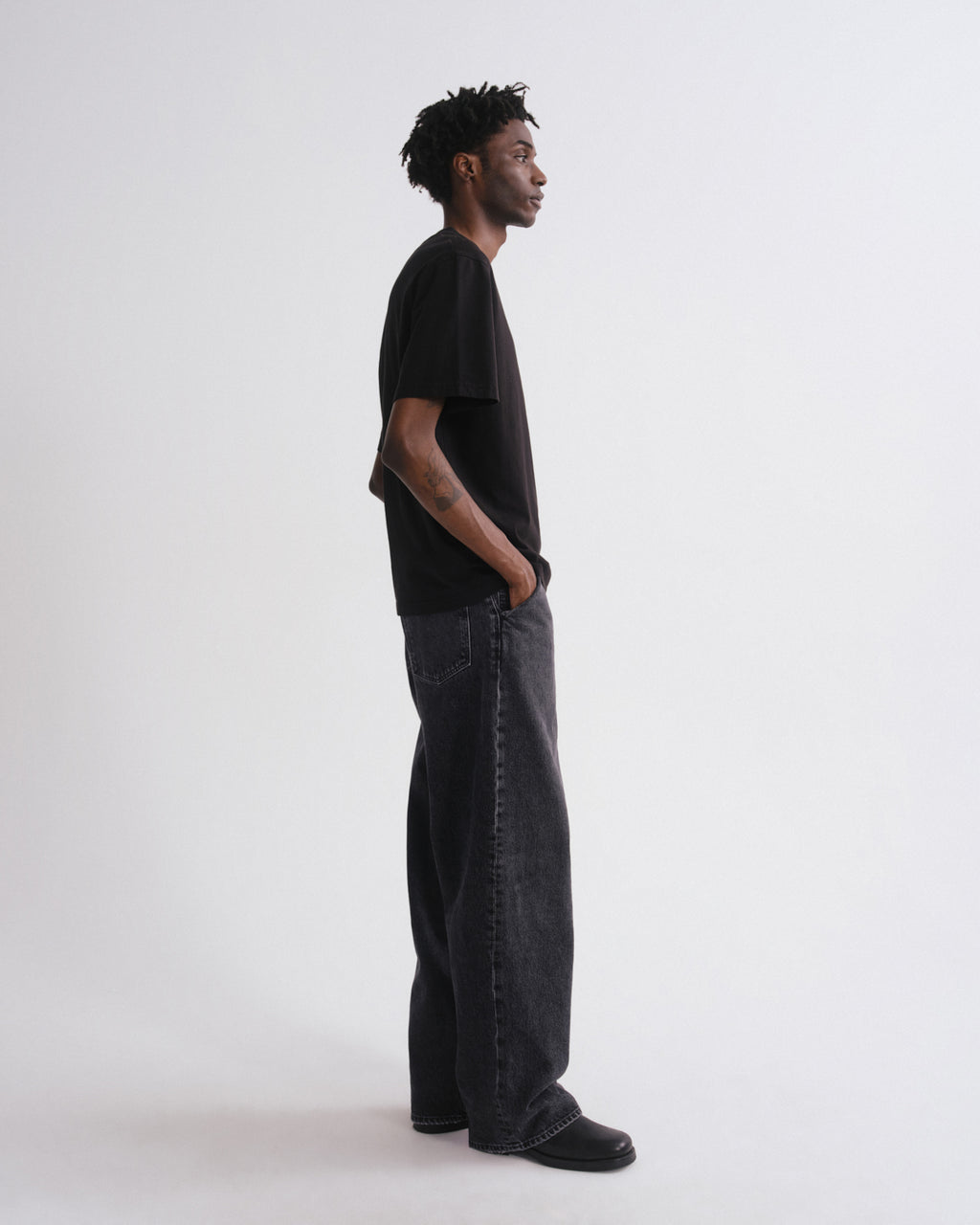 Person wearing a black t-shirt and dark jeans standing against a white background