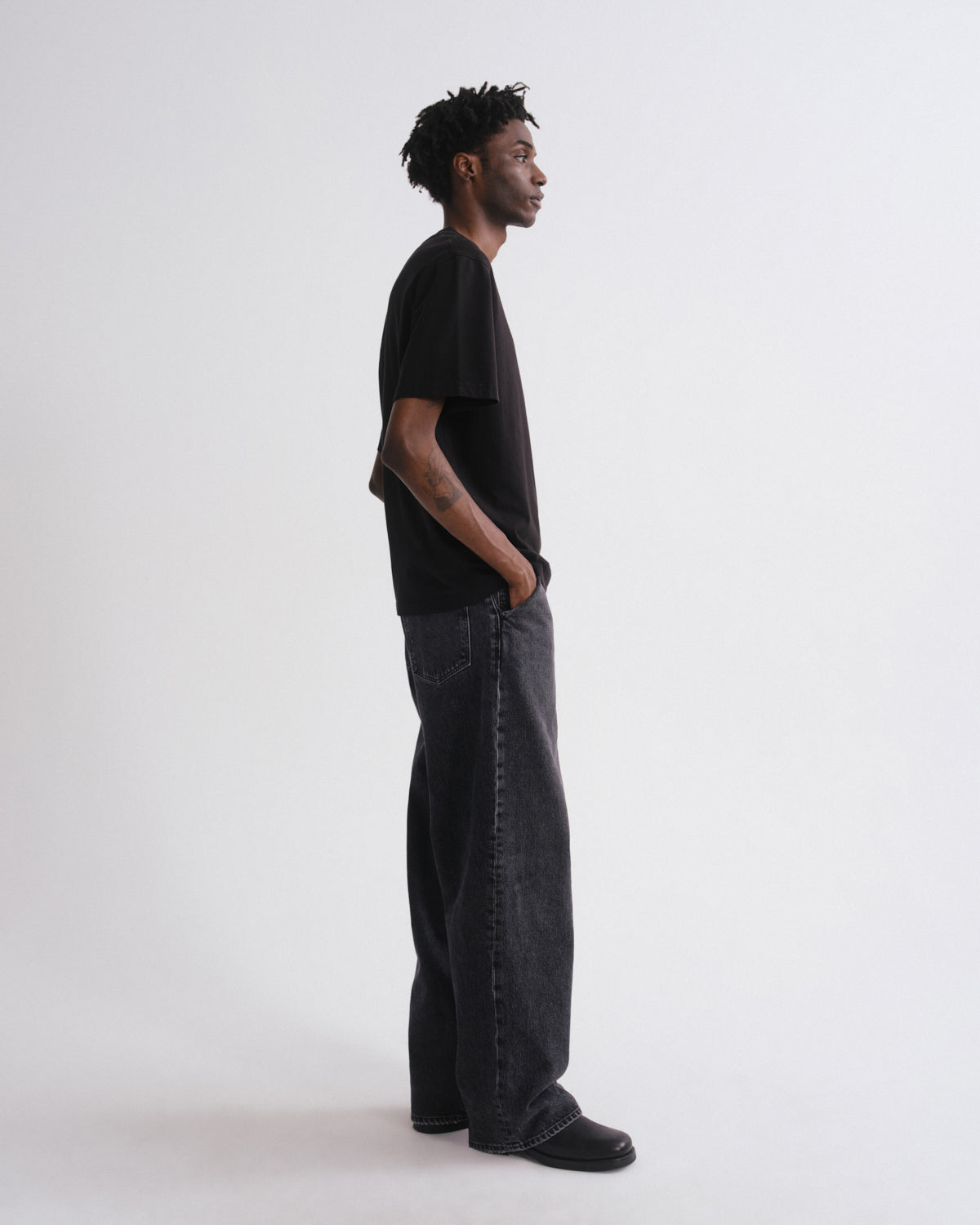 Person wearing a black t-shirt and dark jeans standing against a white background