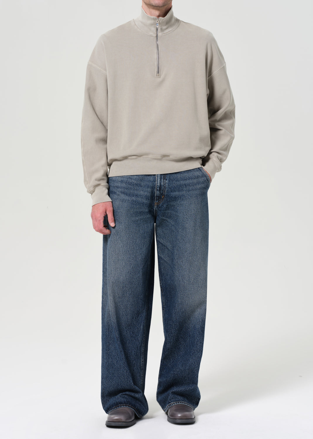 Person wearing a beige sweater and blue jeans on a white background