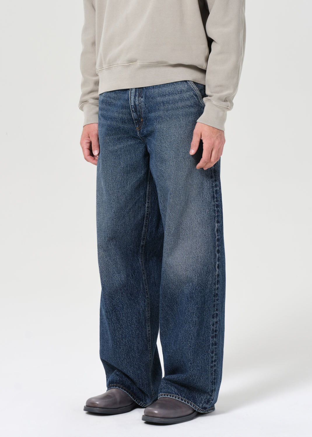 Person wearing blue jeans and a beige sweatshirt on a white background