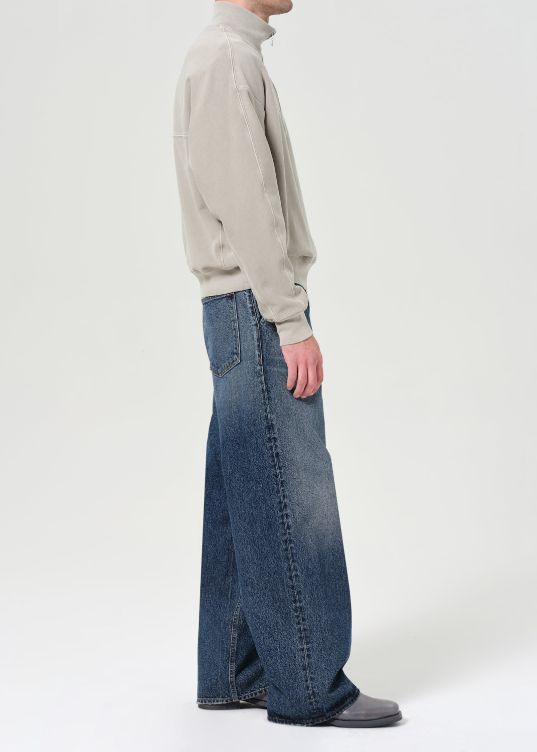 Person wearing a light gray turtleneck and blue jeans on a white background