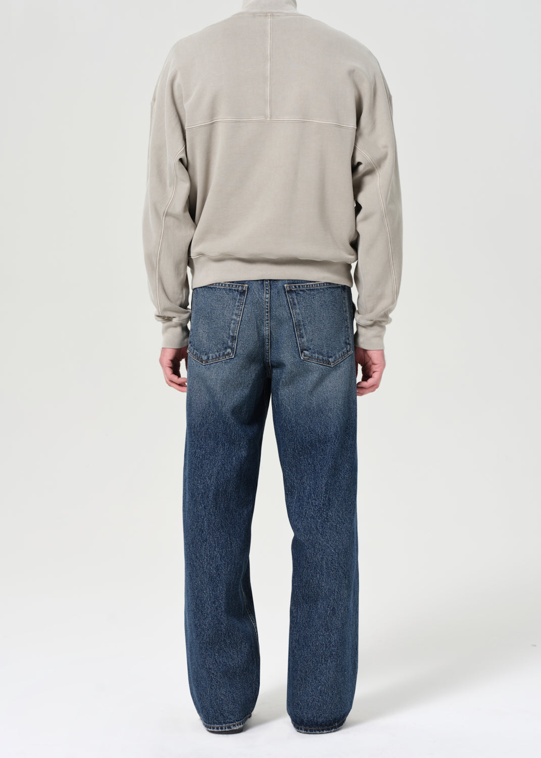 Person wearing a beige sweater and blue jeans on a white background