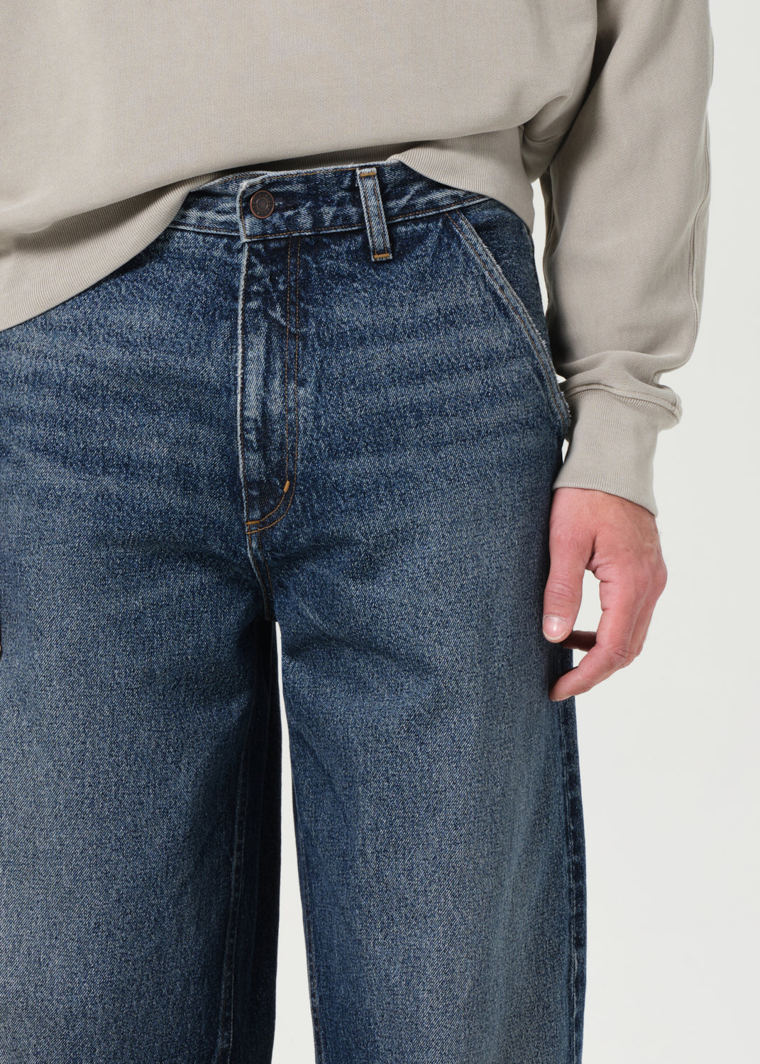 Person wearing blue jeans and a beige sweater on a white background