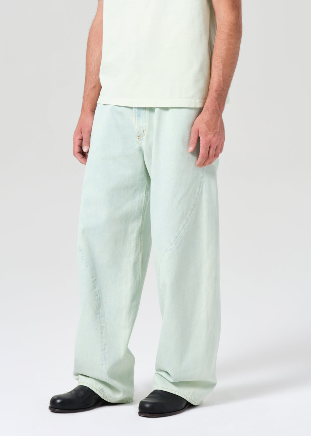 Person wearing light green wide-leg jeans and black shoes on a white background