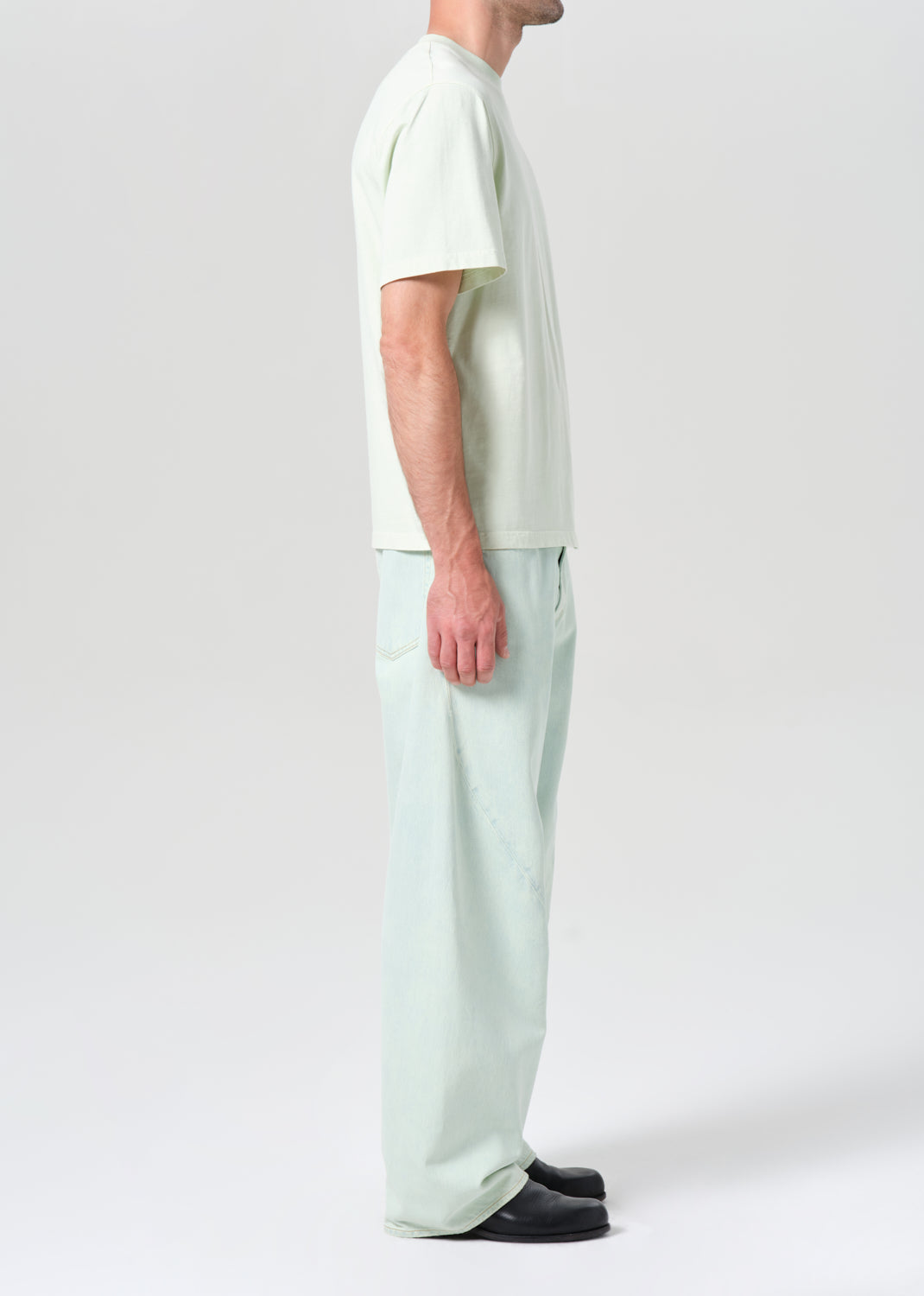 Person wearing a white t-shirt and light green pants on a plain background