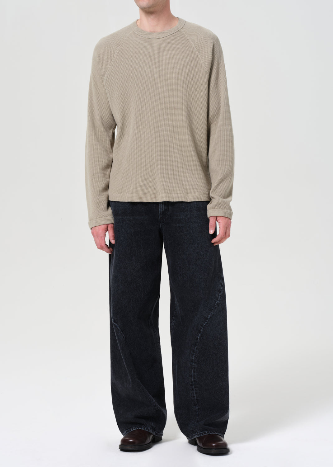 Person wearing a beige sweater and dark jeans on a white background