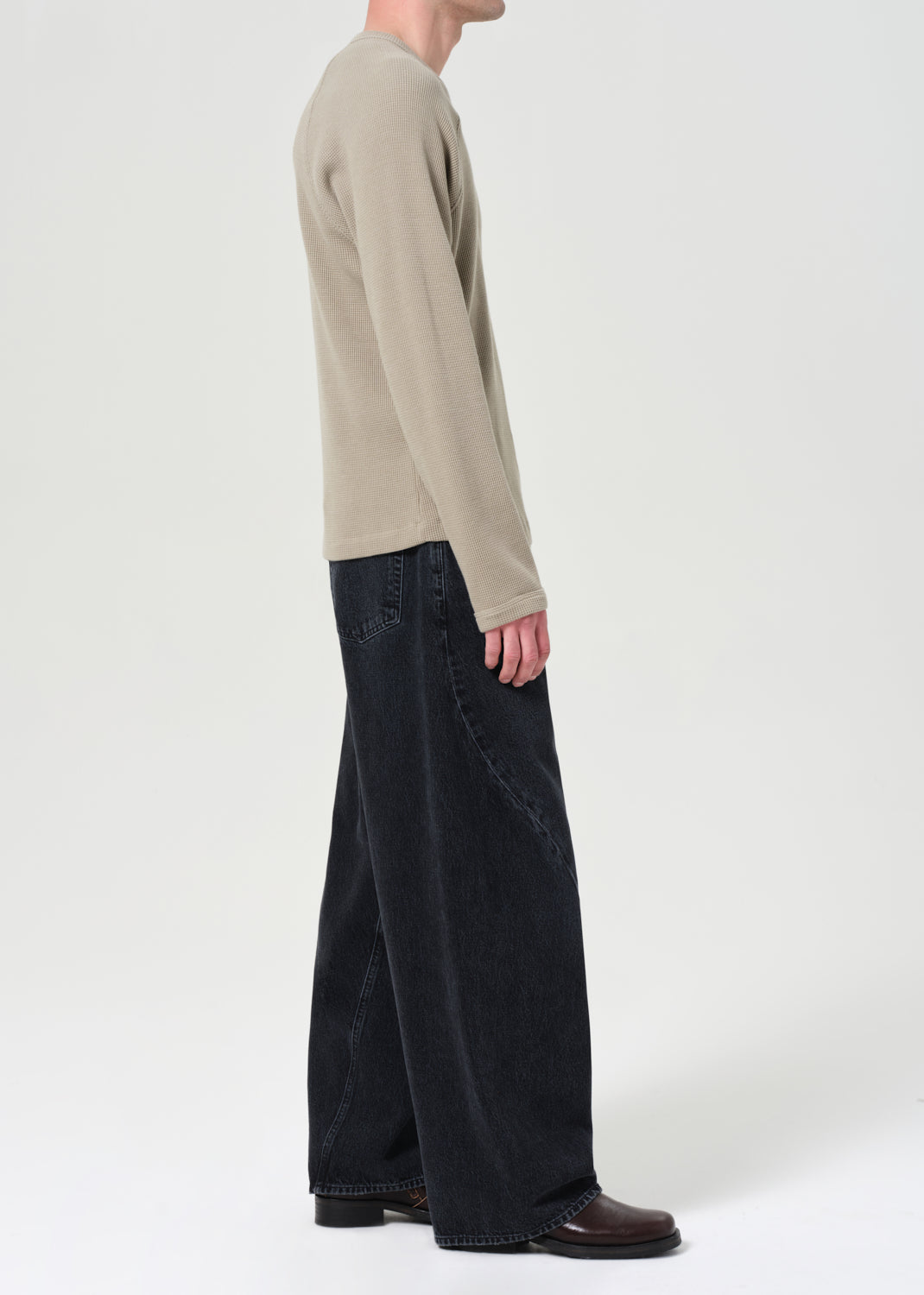 Person wearing a beige long-sleeve shirt and black wide-leg jeans on a white background