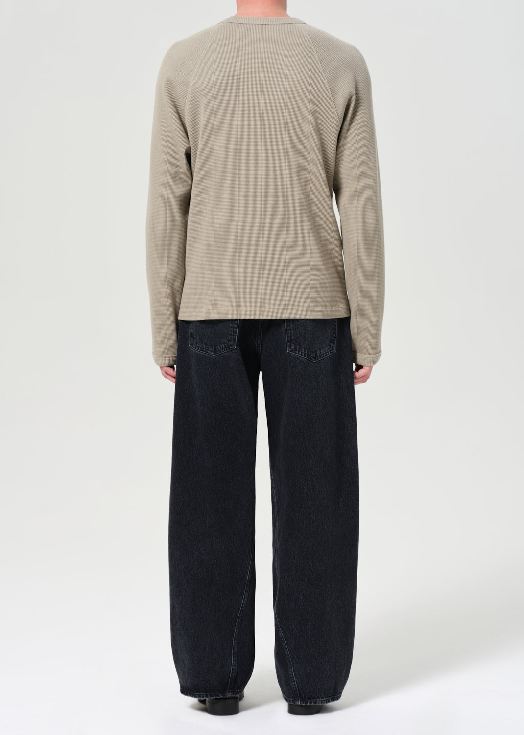 Person wearing a beige sweater and black pants on a white background