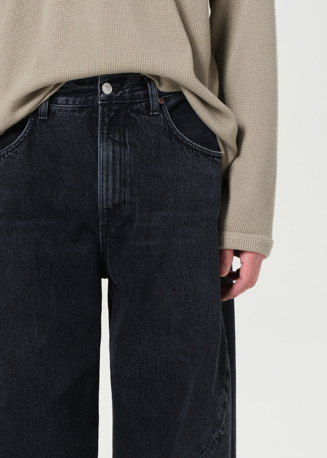 Person wearing black jeans and a beige sweater on a white background