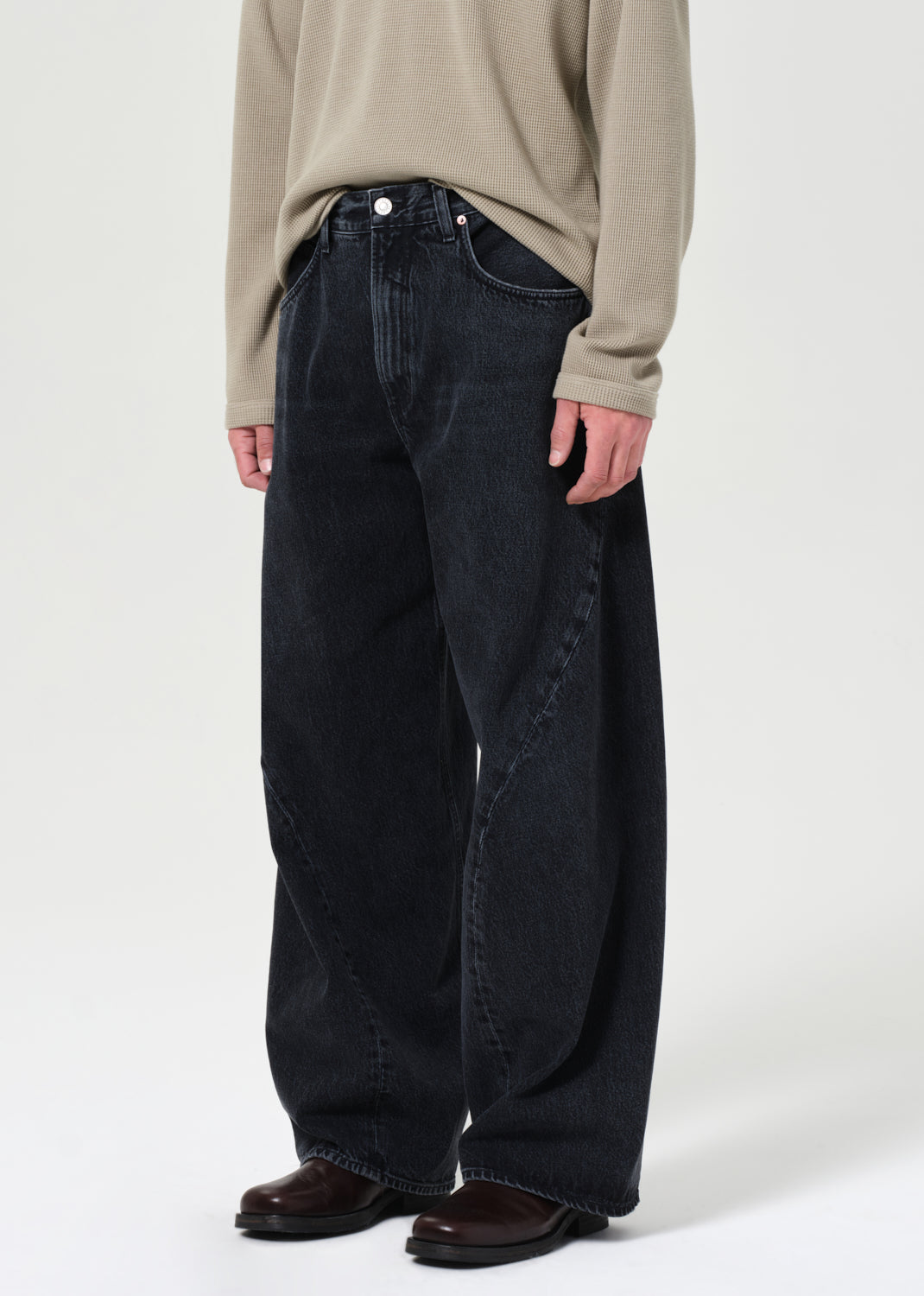 Person wearing dark jeans and a beige sweater on a plain background