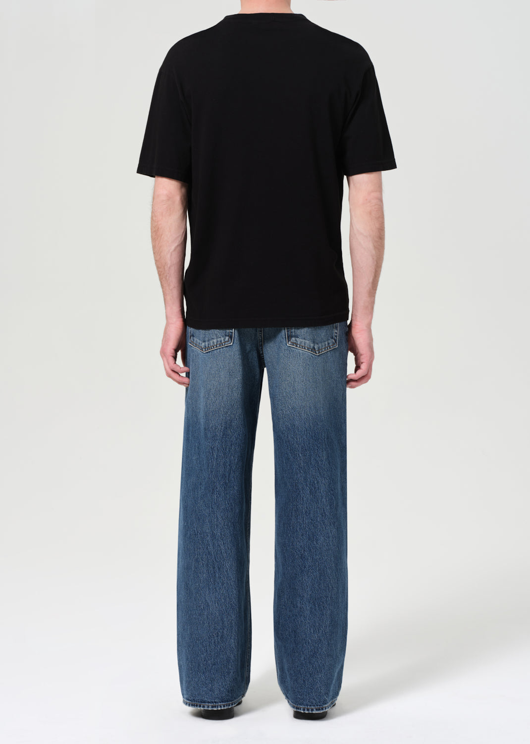 Person wearing a black t-shirt and blue jeans on a white background