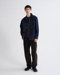 Person wearing a dark denim jacket and black pants on a white background