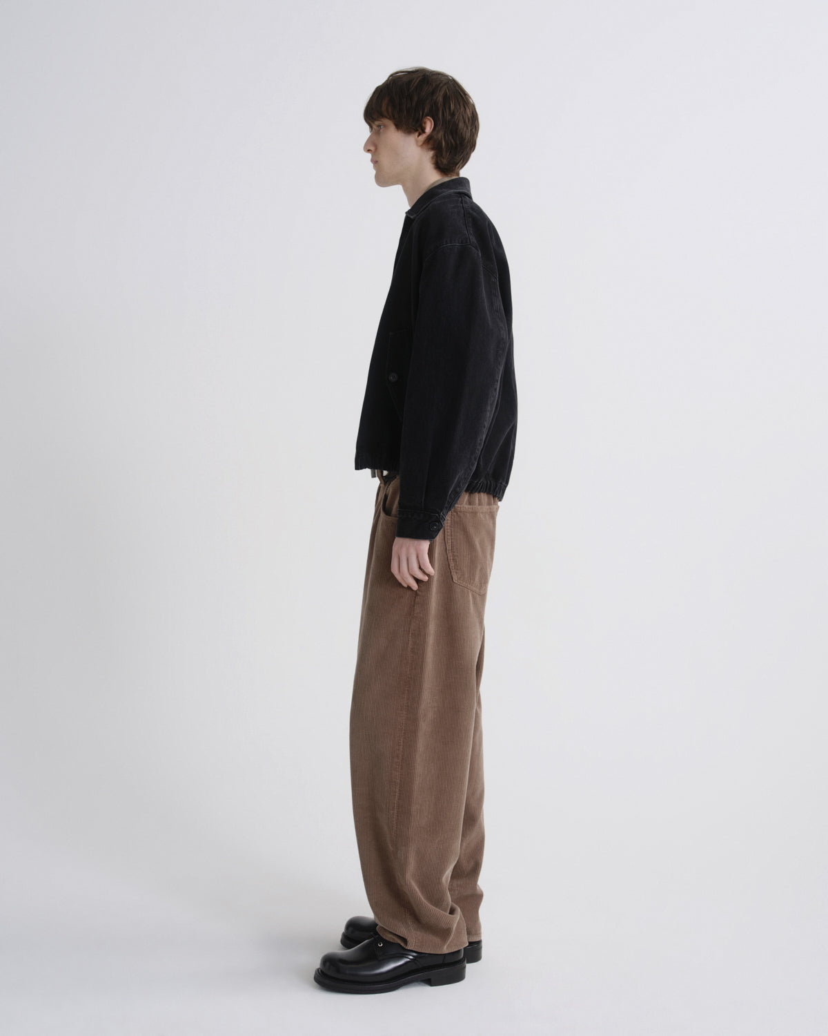 Person wearing a black shirt and brown pants on a grey background