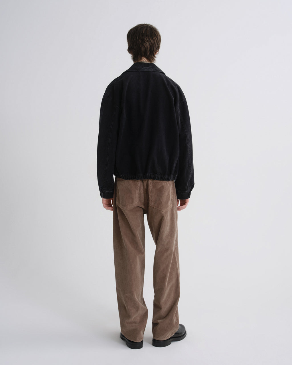 Person wearing a black jacket and brown pants on a grey background