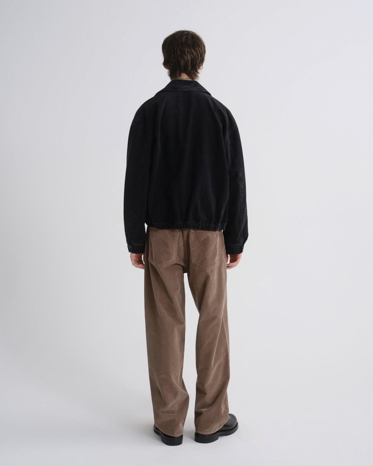 Person wearing a black jacket and brown pants on a grey background