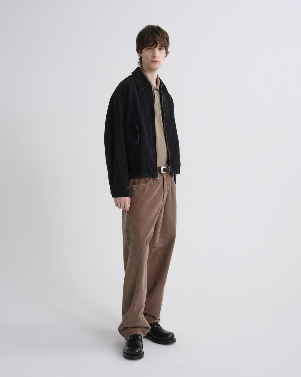 Person wearing a black jacket, beige shirt, and brown pants on a grey background