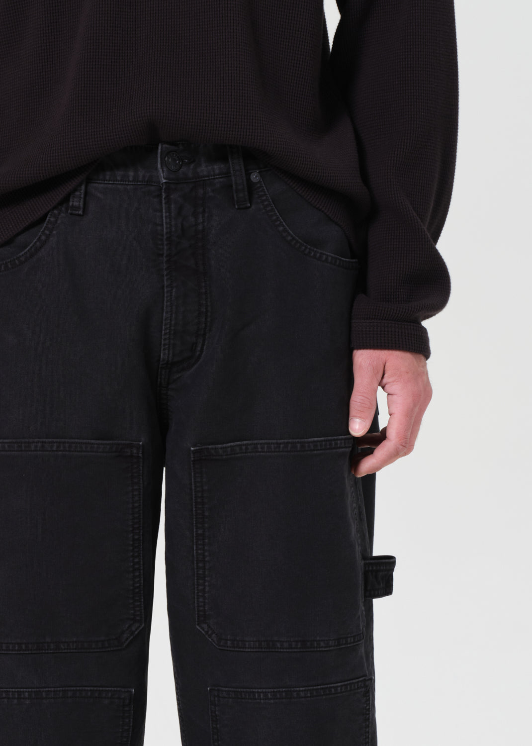 Person wearing black cargo pants and a black sweatshirt on a light gray background