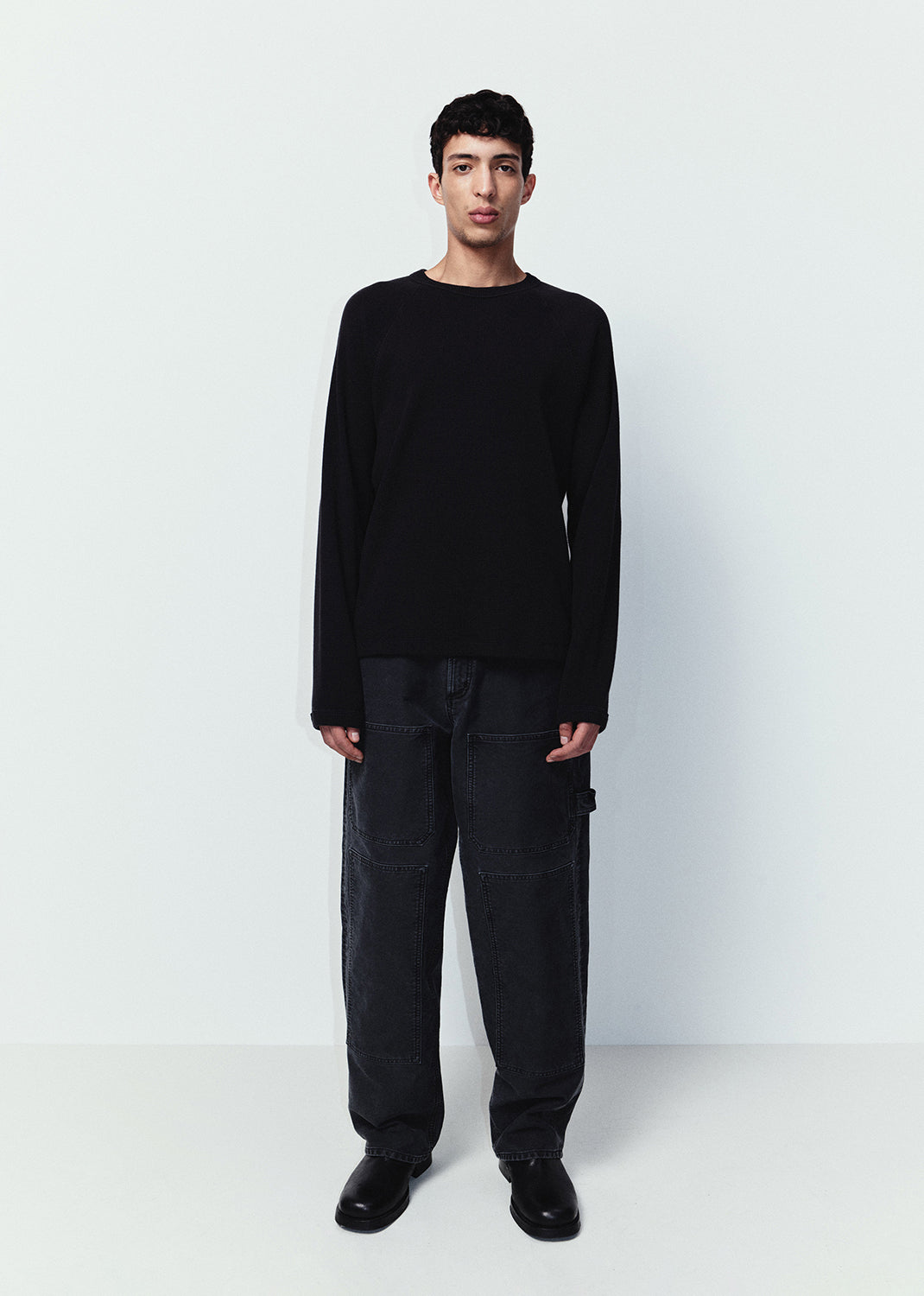 Man wearing a black sweater and pants standing against a white background