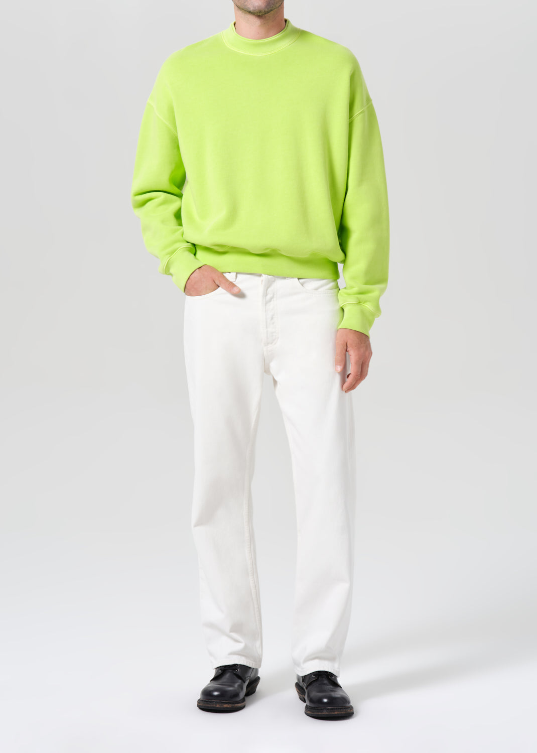 Person wearing a bright green sweater and white pants on a white background