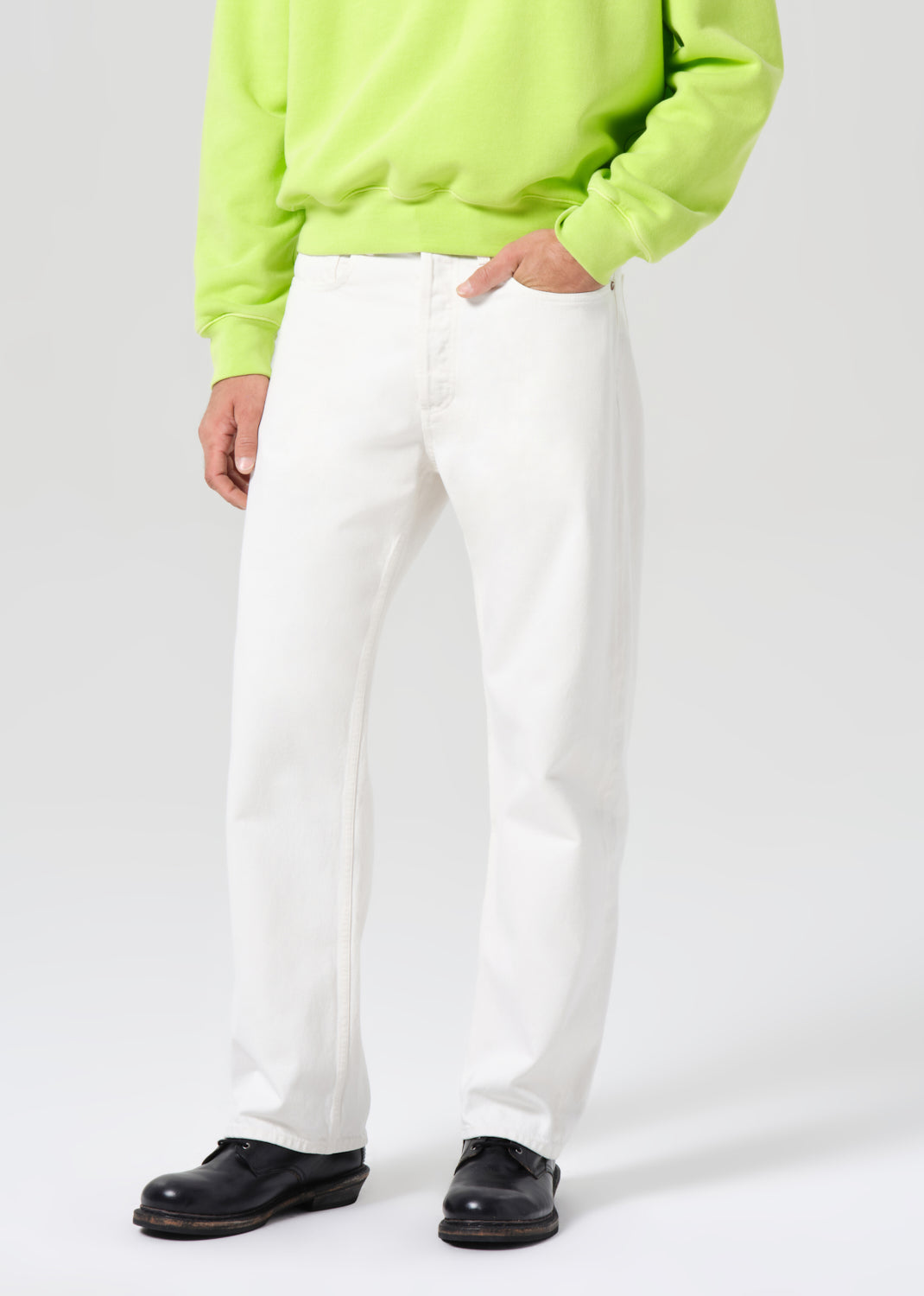 Person wearing a bright green sweatshirt, white pants, and black shoes on a white background