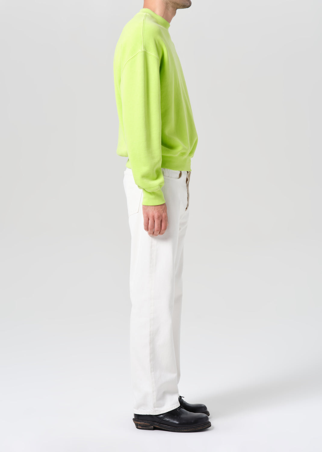 Person wearing a bright green sweater and white pants on a plain background