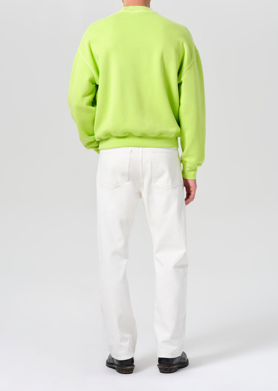 Person wearing a bright green sweater and white pants on a plain background