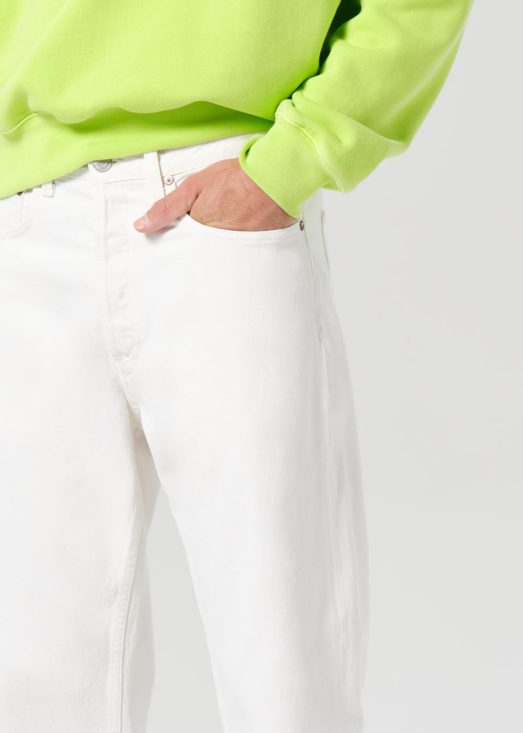 Person wearing a bright green sweatshirt and white pants on a light gray background